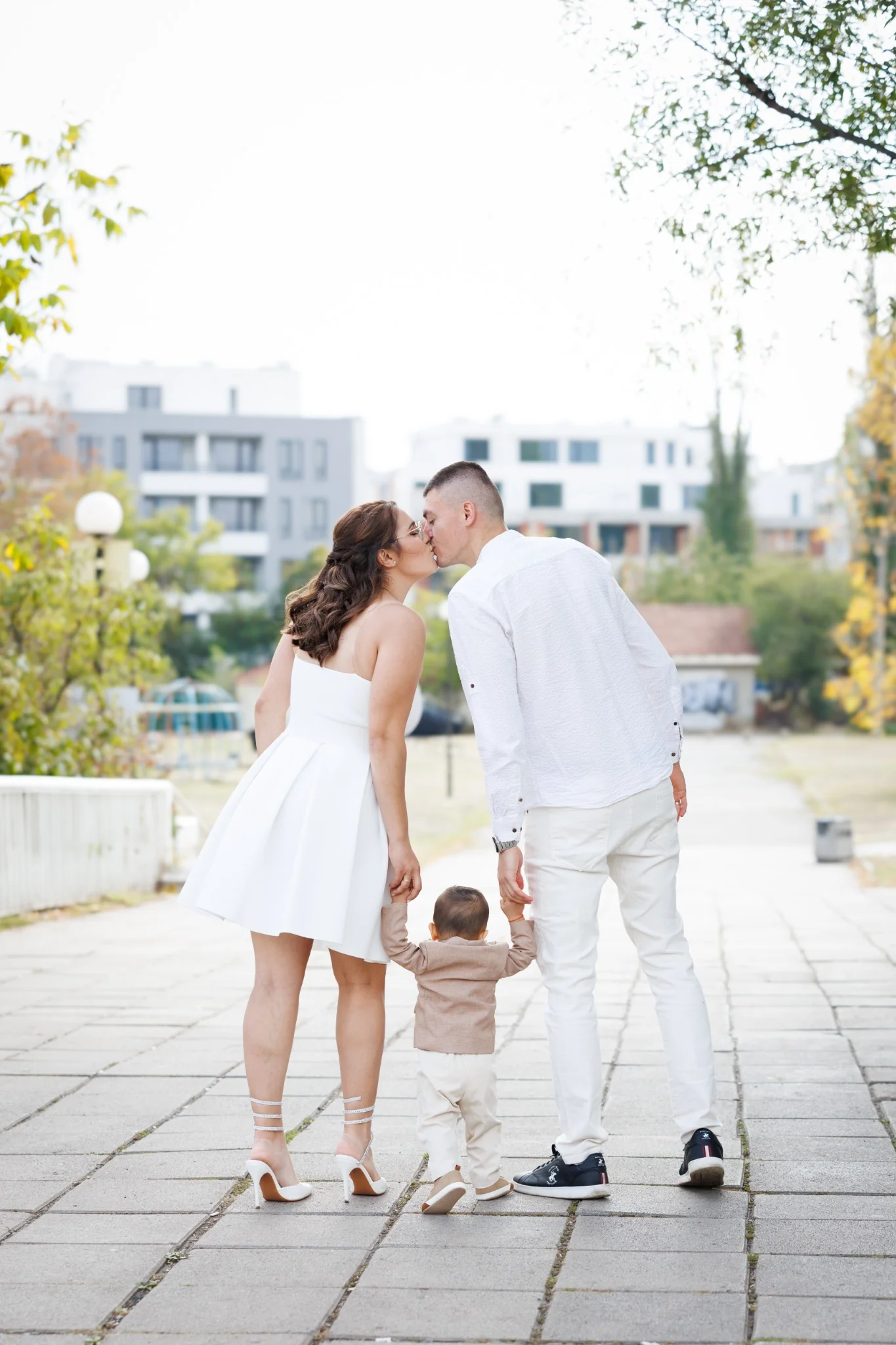 Семейна фотосесия – родители целуват детето по време на разходка